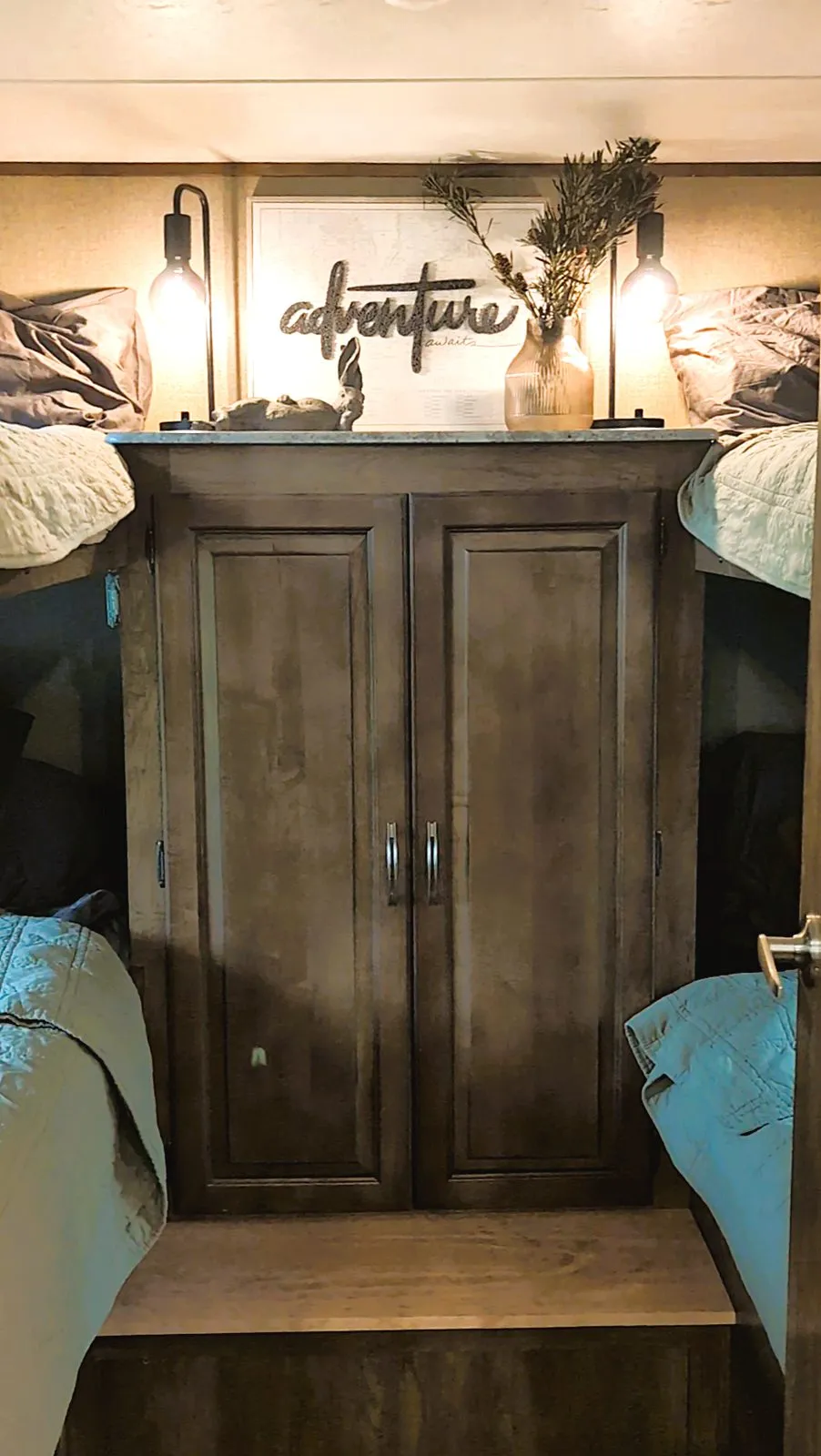 Inside the rental camper: a wooden wardrobe between two beds, under an “adventure” sign