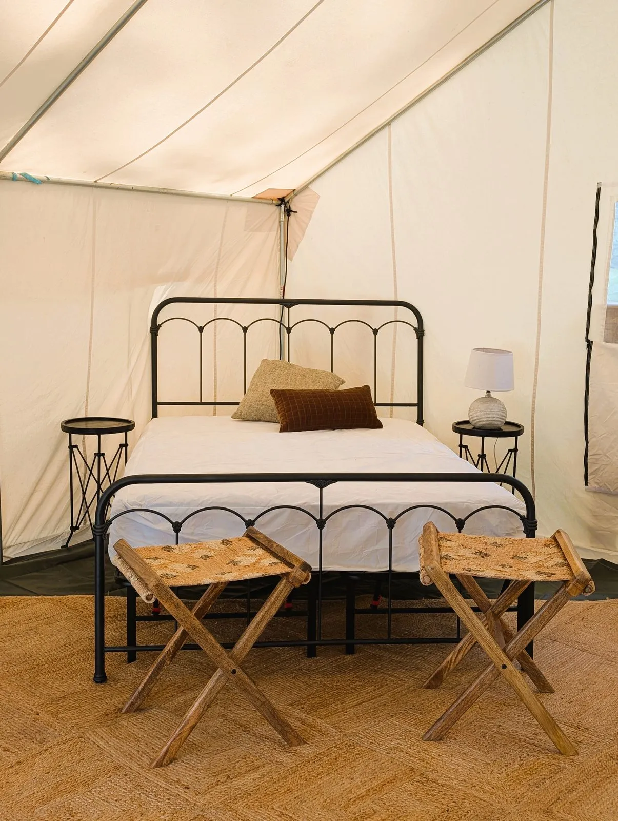 Inside the glamping tent: an iron-frame queen bed between two side tables and lamps