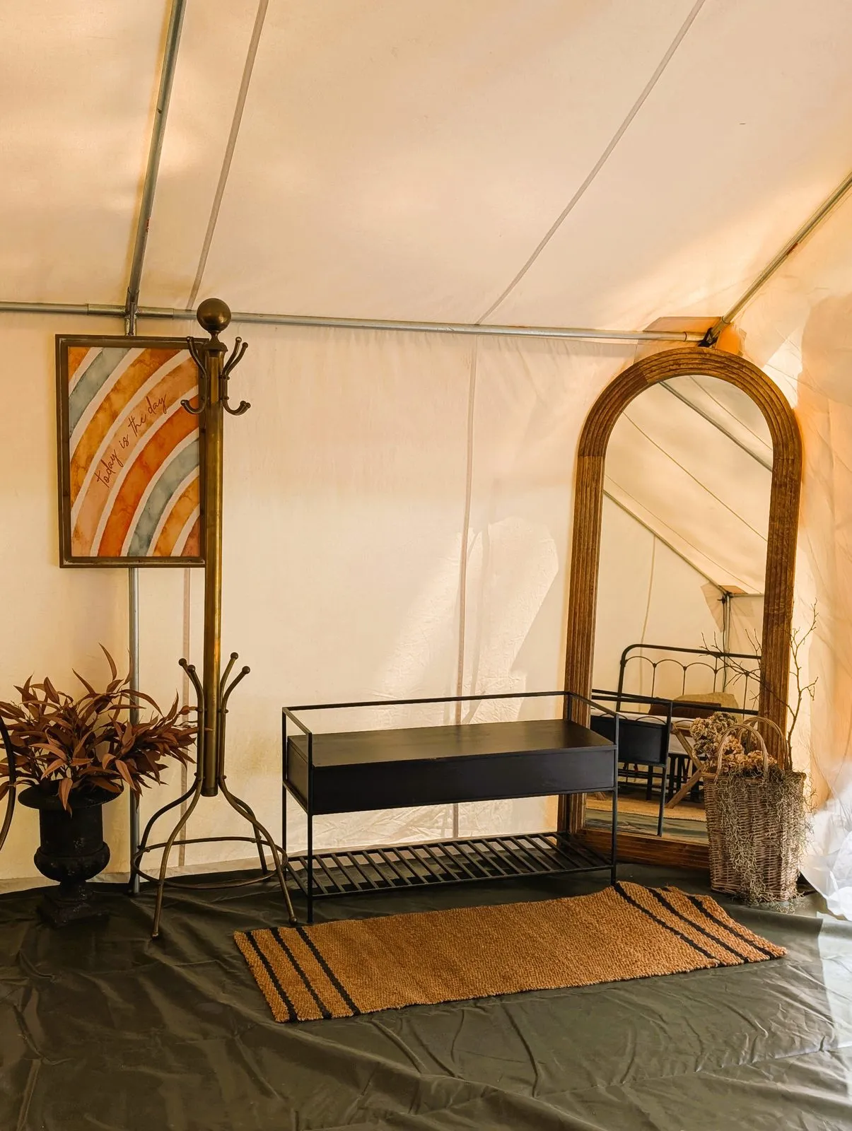 Inside the glamping tent: a coat rack, an arched mirror and a bench on a woven rug