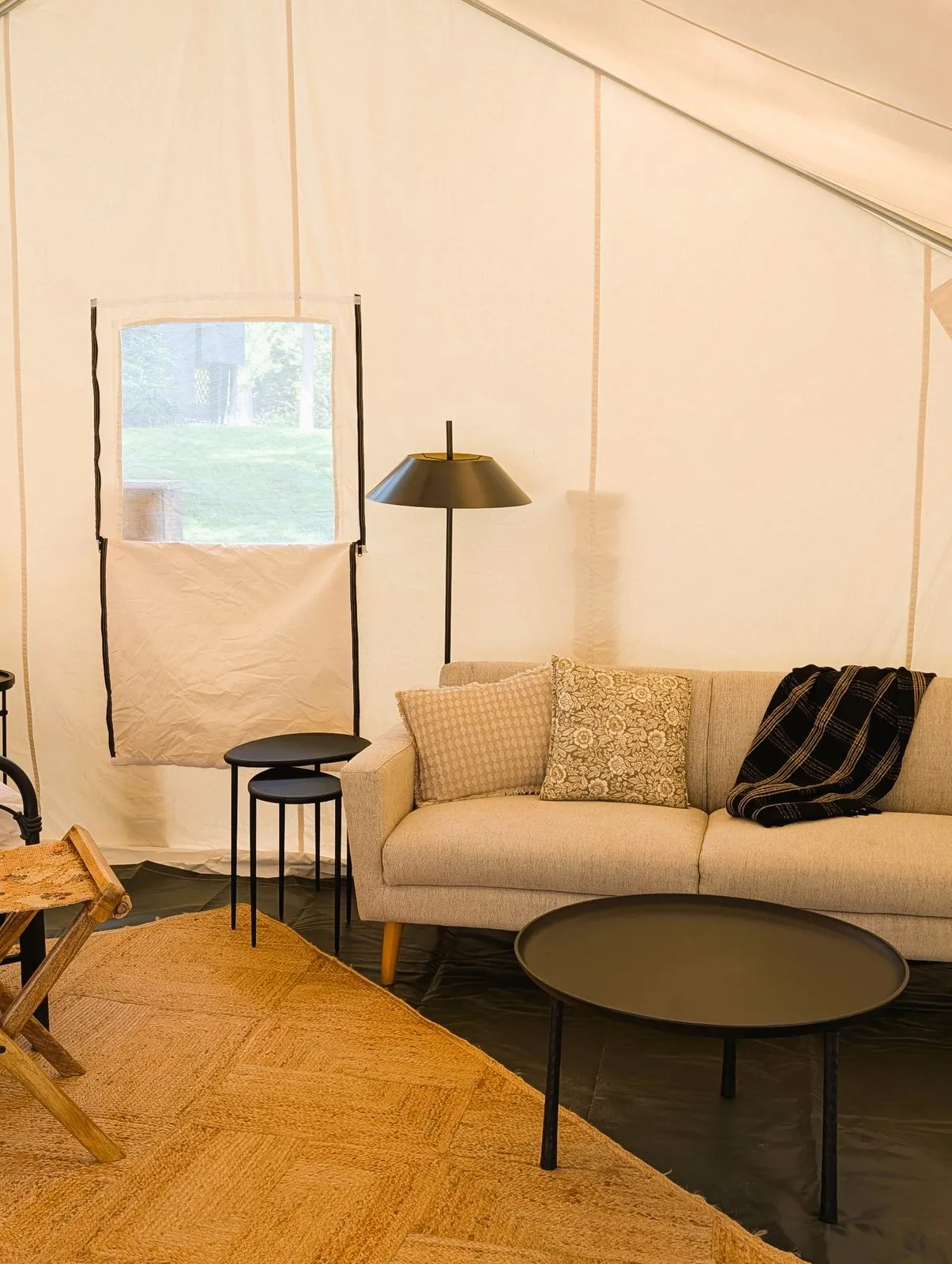 Inside the glamping tent: a sofa with pillows and a throw, a round coffee table and a floor lamp