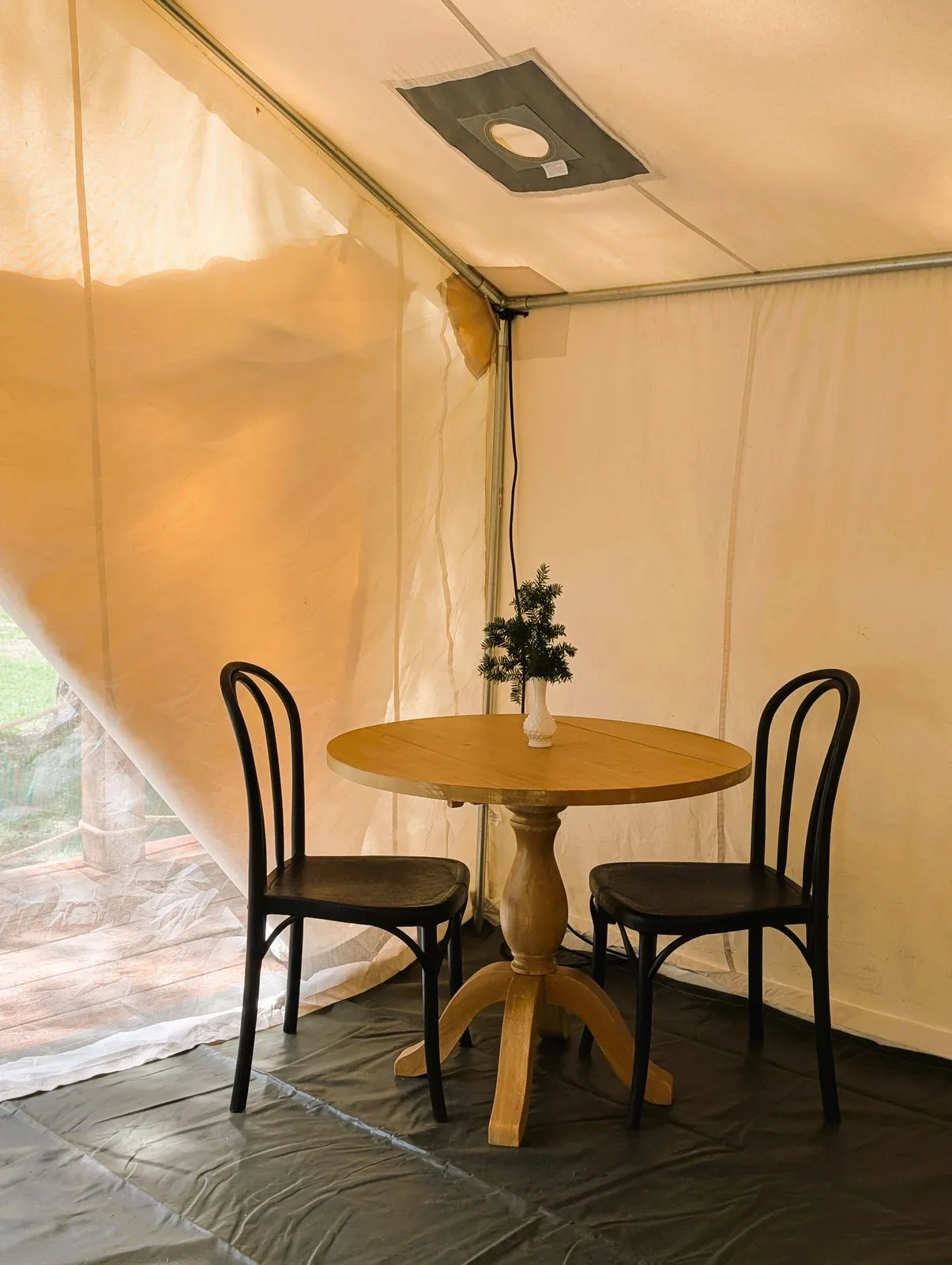Inside the glamping tent: a small round wooden table with two bentwood chairs
