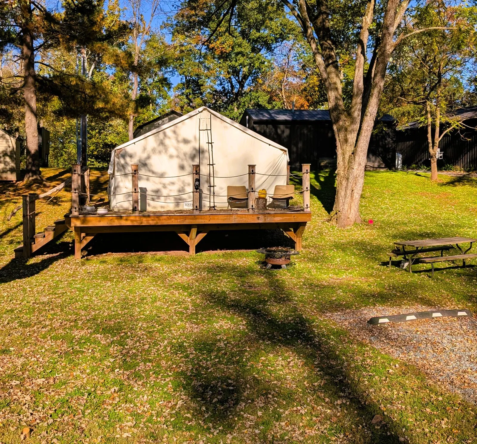 The canvas glamping tent on its wooden deck, with a fire ring in front and a picnic table beside it