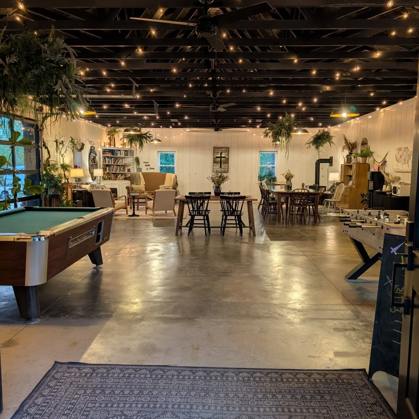 The lodge game room under string lights, with a pool table, foosball, reading nook and long dining tables