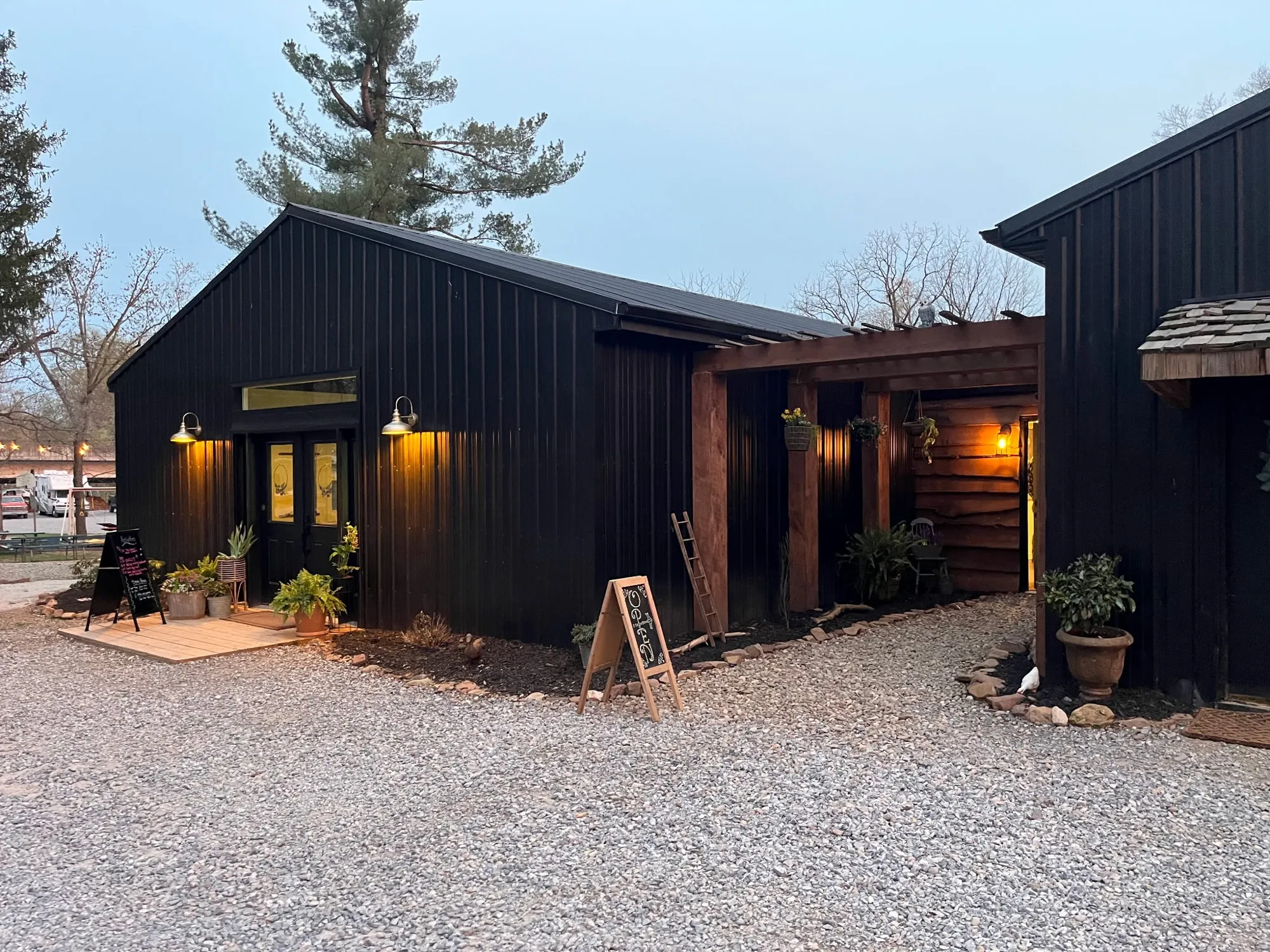 The rec room at dusk, its windows lit, beside the pergola and a chalkboard sign
