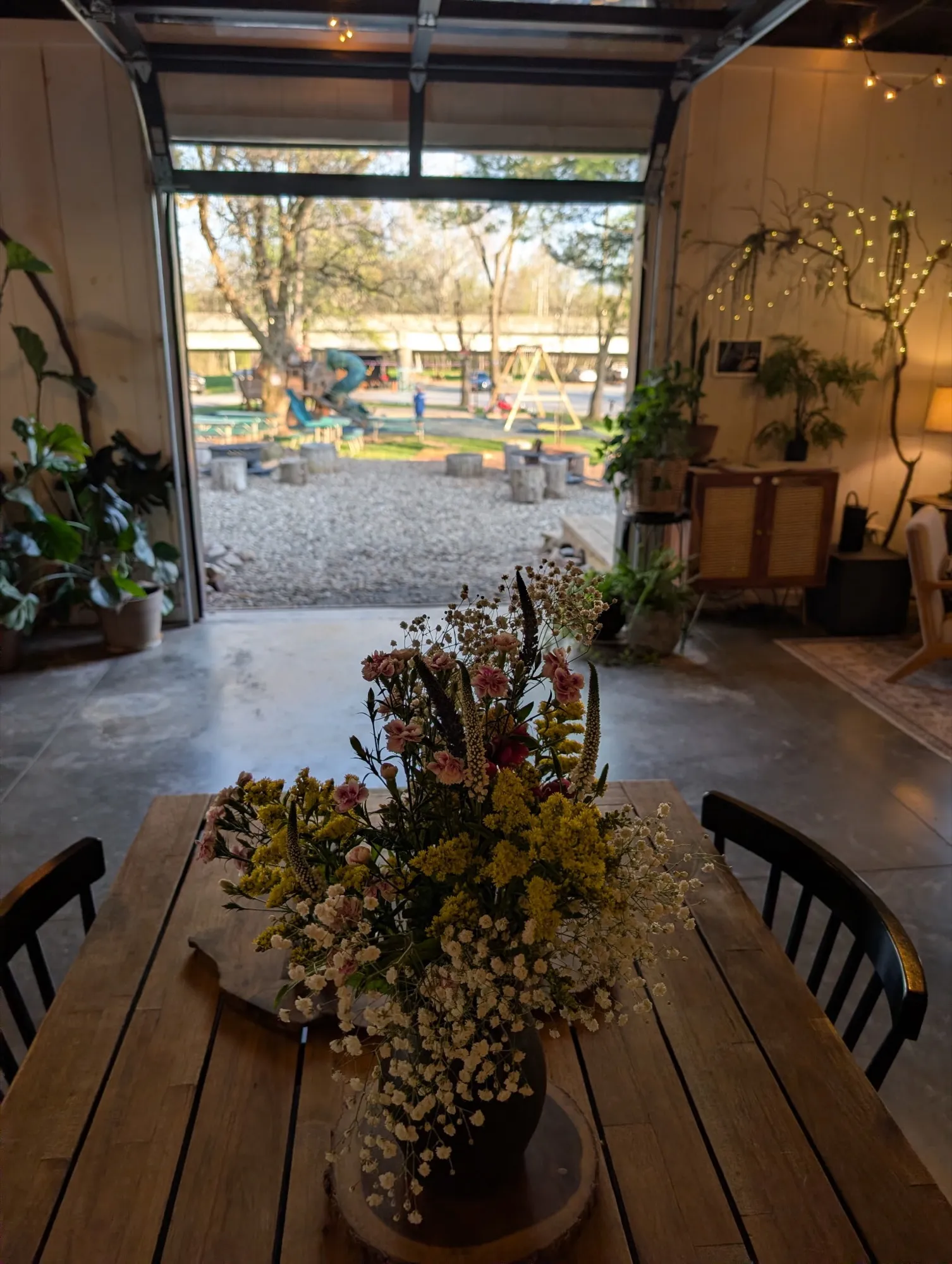 A wildflower centerpiece on a wood table, with the rec room's garage door rolled open to the campground