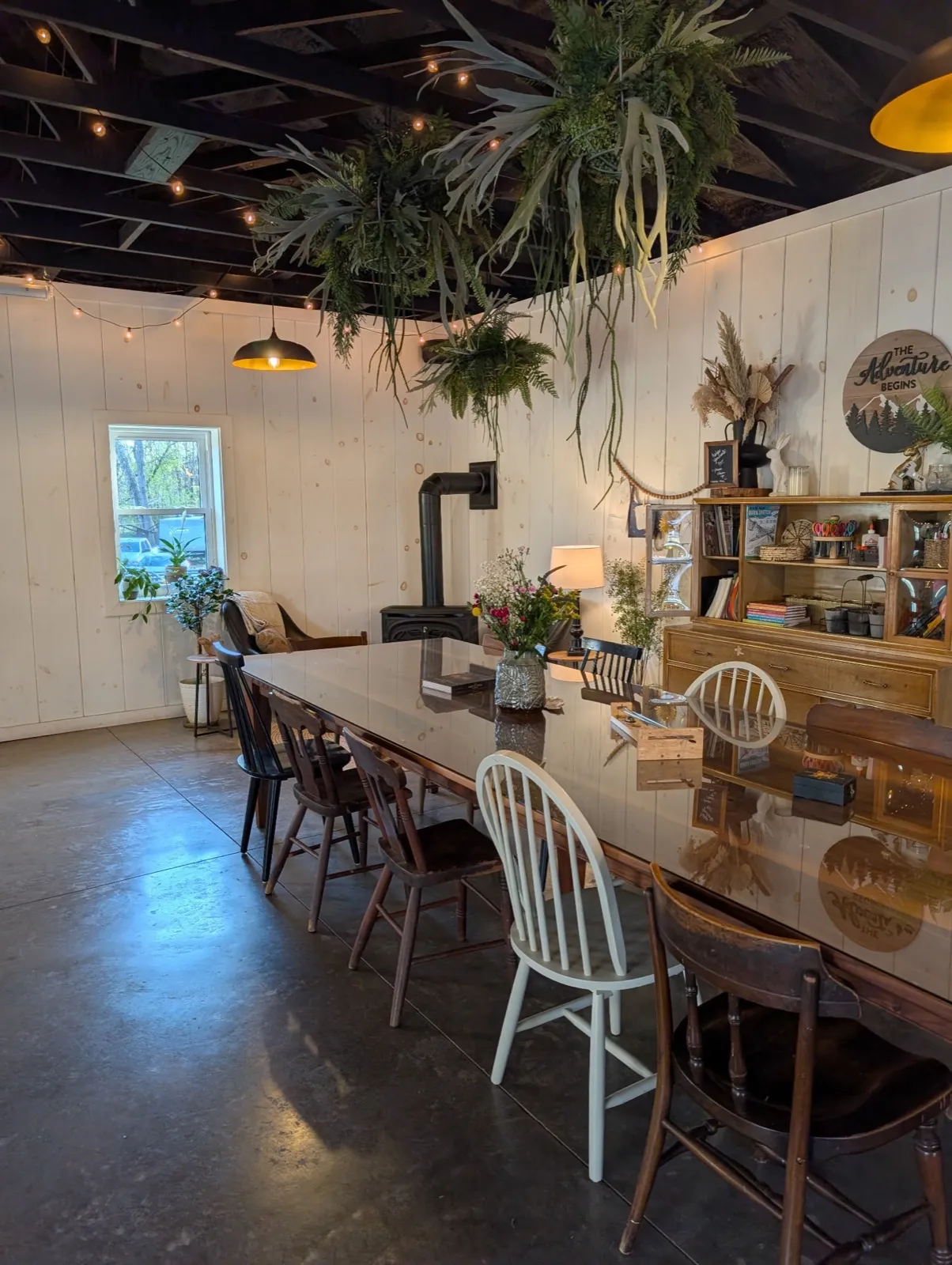 A long farm table with wooden chairs beside the rec room’s wood stove