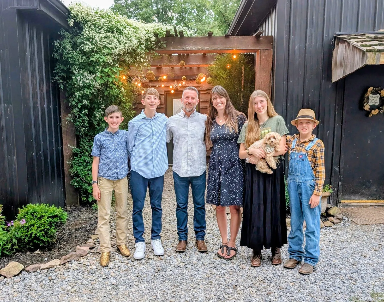 The Thomas family standing together on the gravel by the string-lit pergola